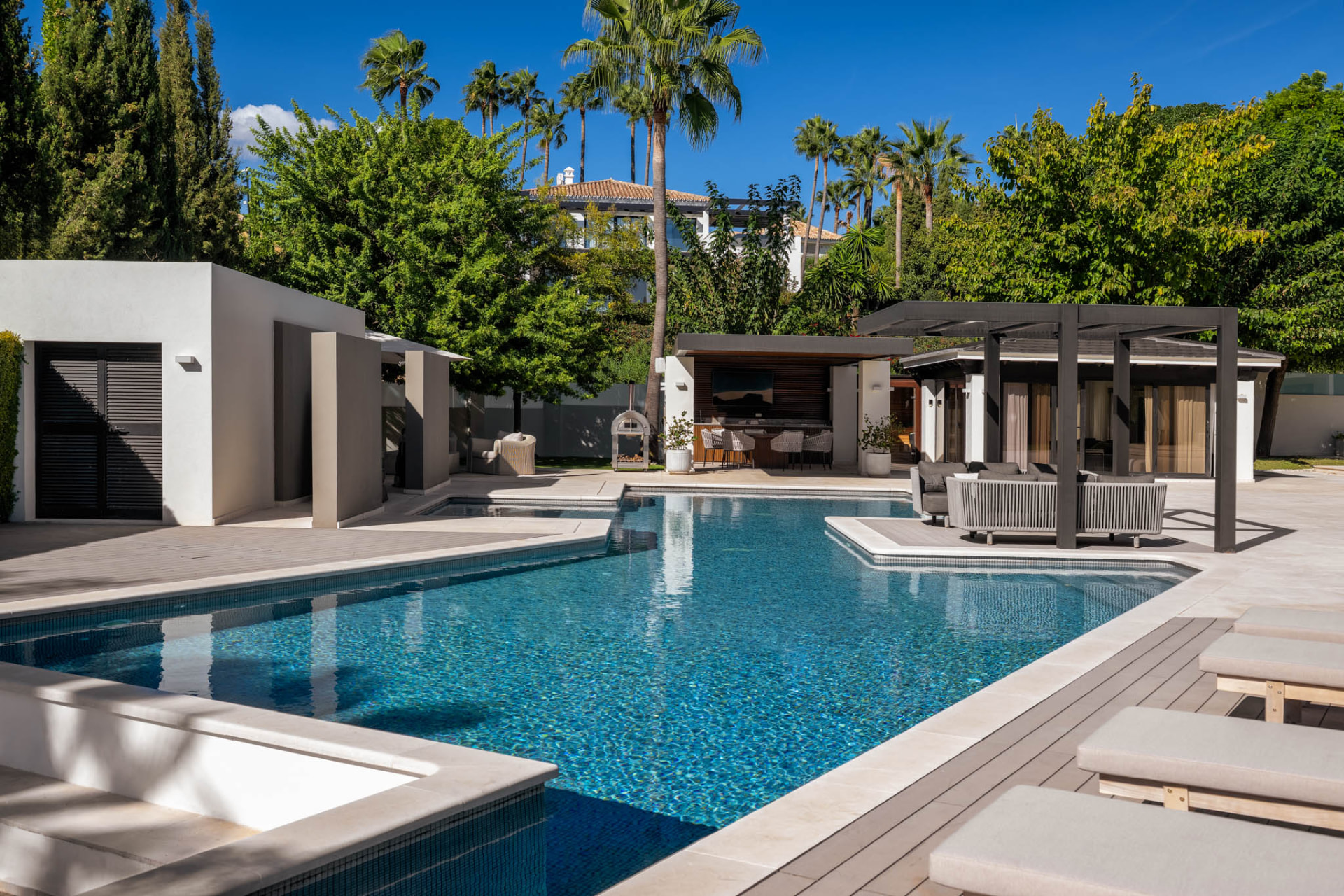 The swimming pool with its lounge platform, looking towards the covered outdoor entertaining structures and palms.