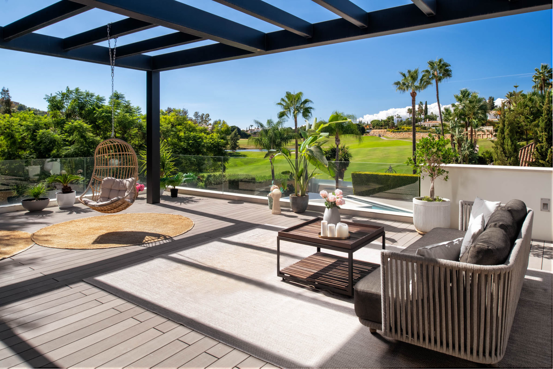 The upper lounge terrace beneath a dark pergola, with open views across the golf course.